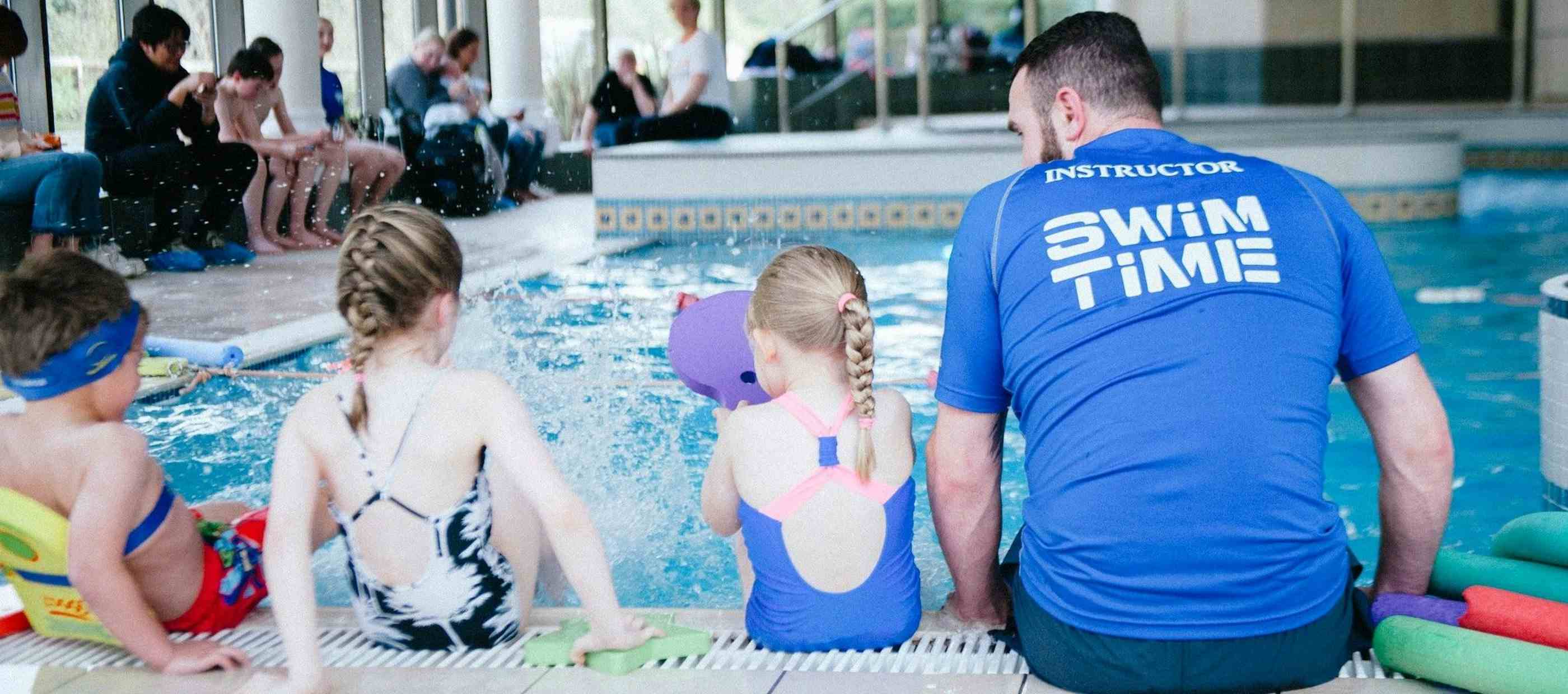 Swimming instructor and children sitting on side of pool