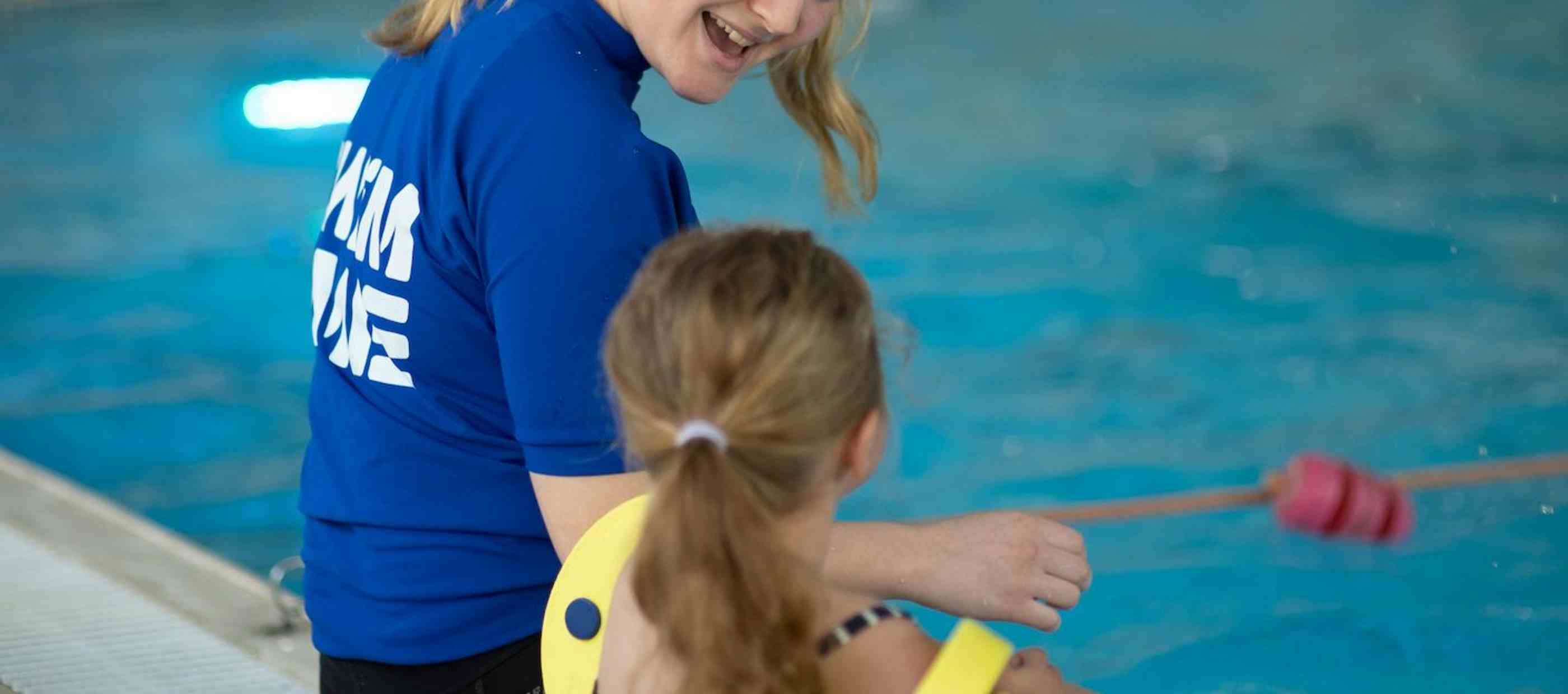 Swimming instructor and child sitting on side of pool
