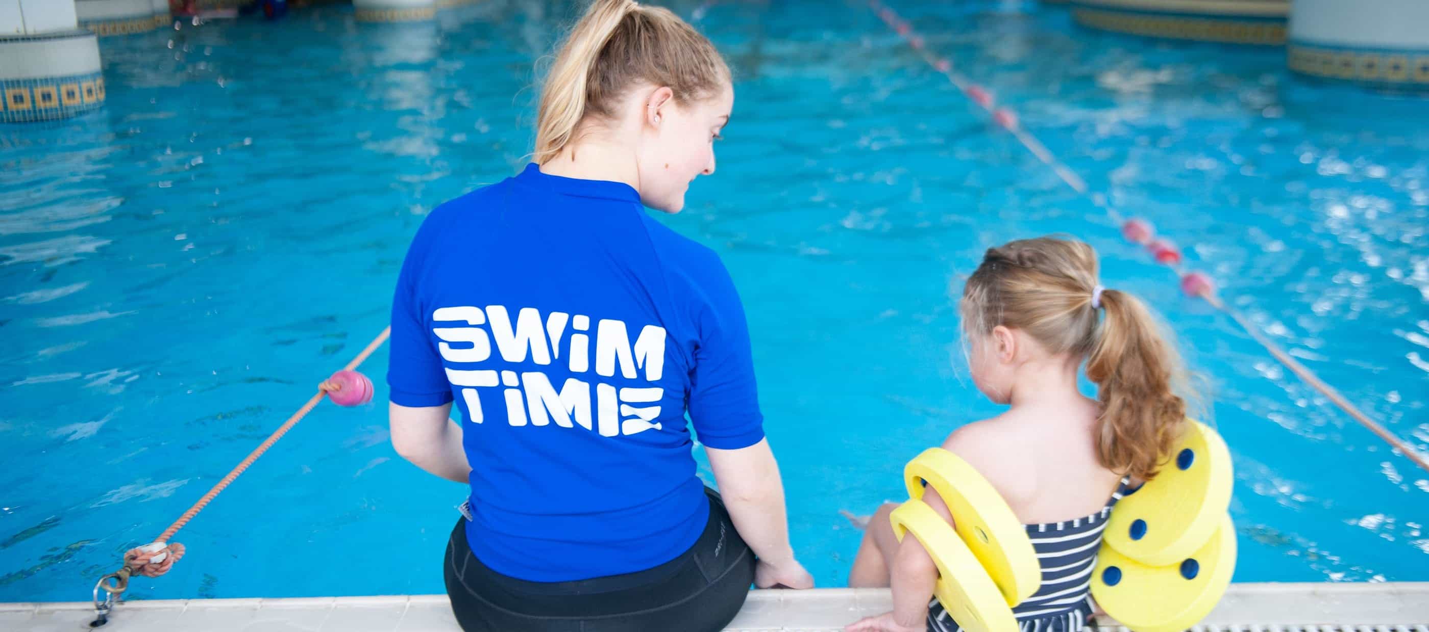 Swimming instructor and child sitting on side of pool