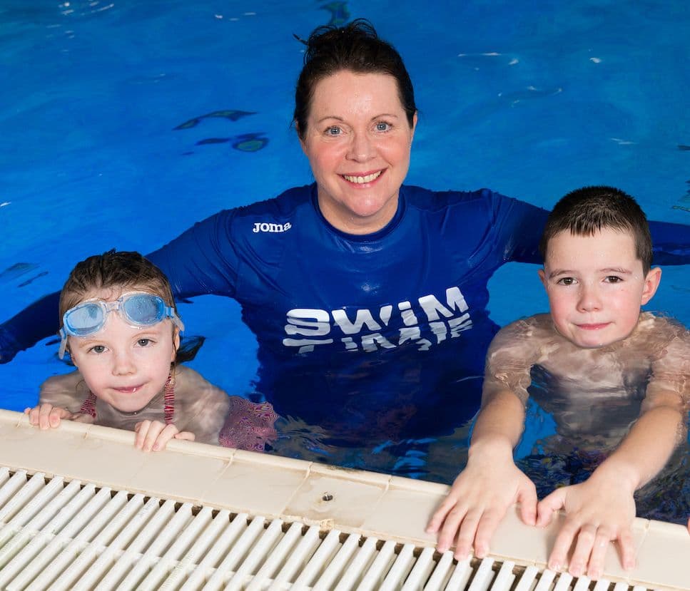 Instructor and children resting on side of swimming pool