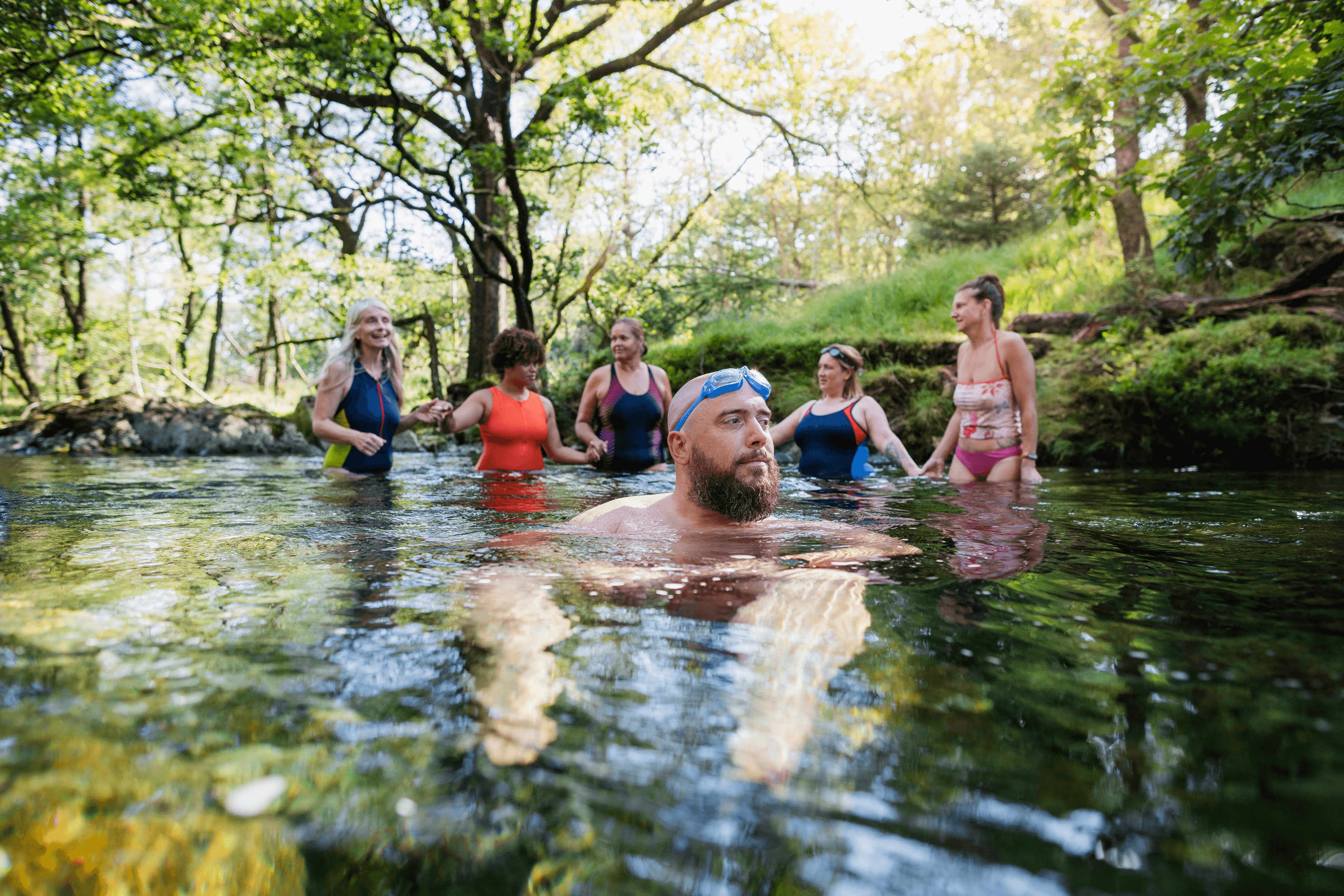 Group of friends enjoying wild swimming in woodland river
