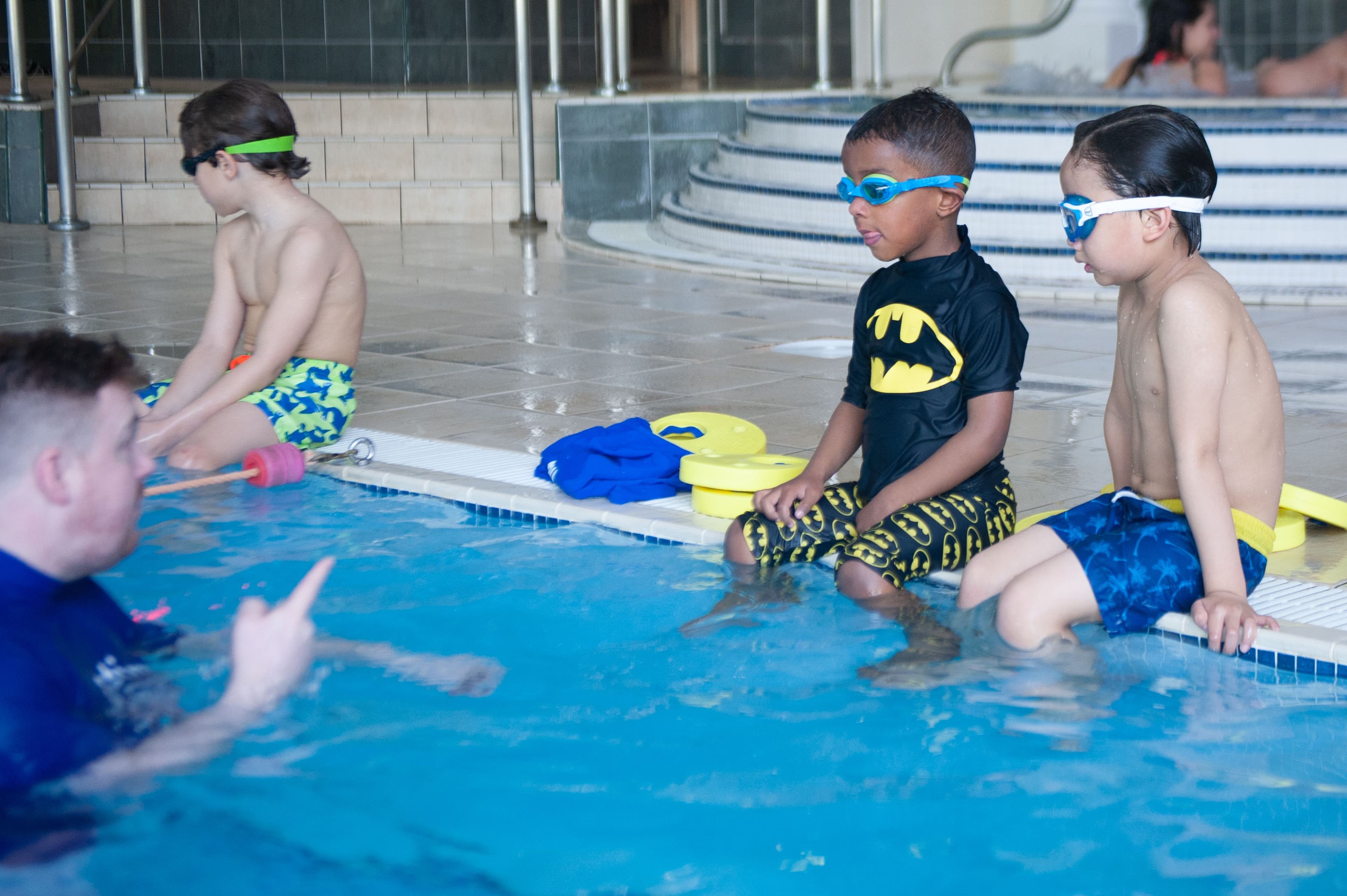 Children sitting on side of pool listening to Instructor
