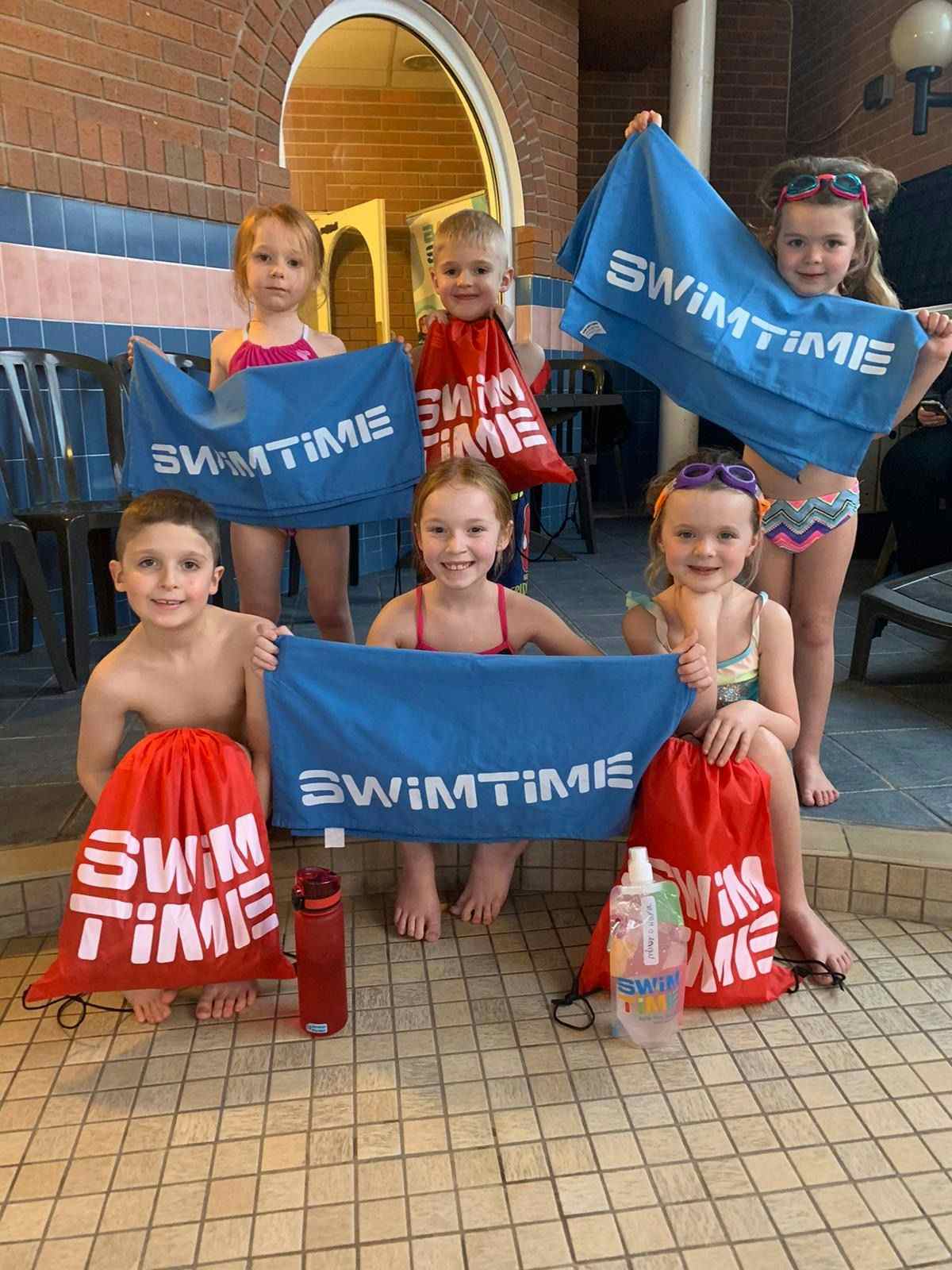 Children holding bags and towels with Swimtime logo