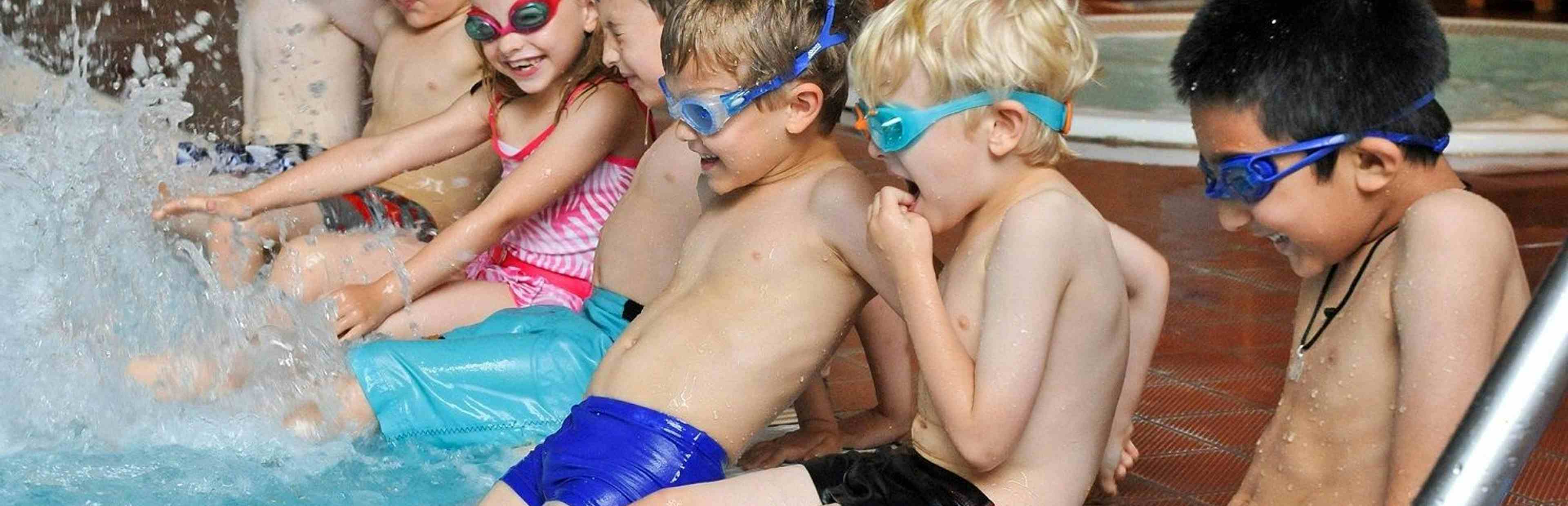 Children sitting on side of pool kicking their legs