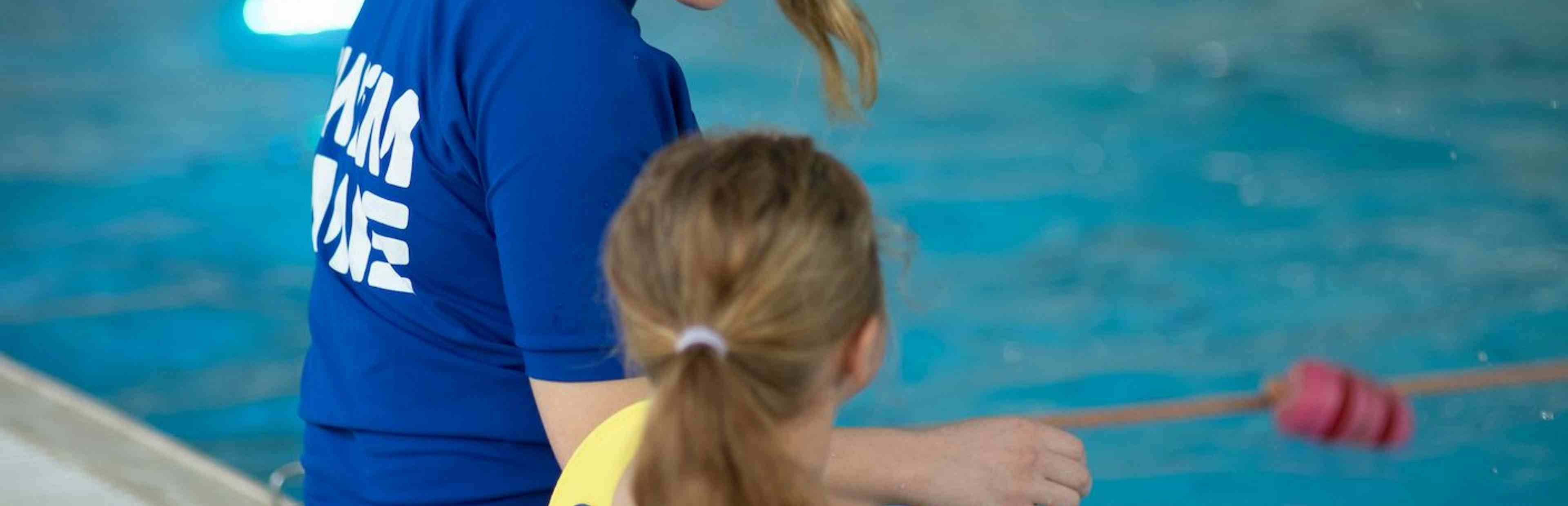Swimming instructor and child sitting on side of pool