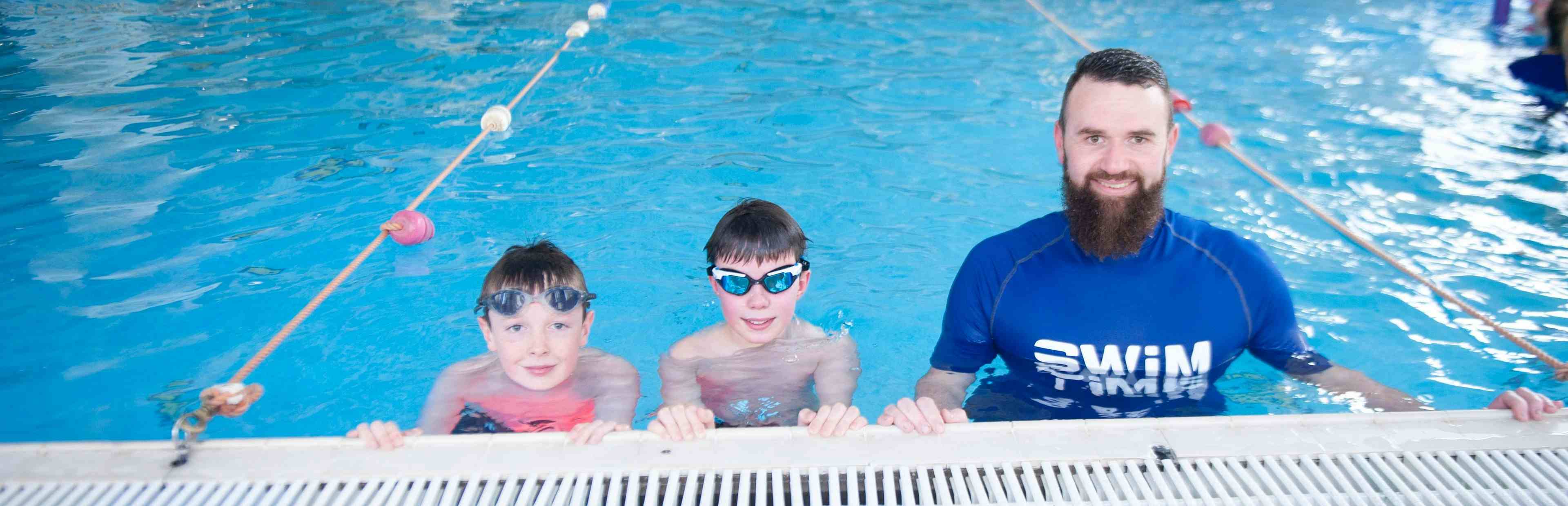 Swimming instructor and children resing on side of pool