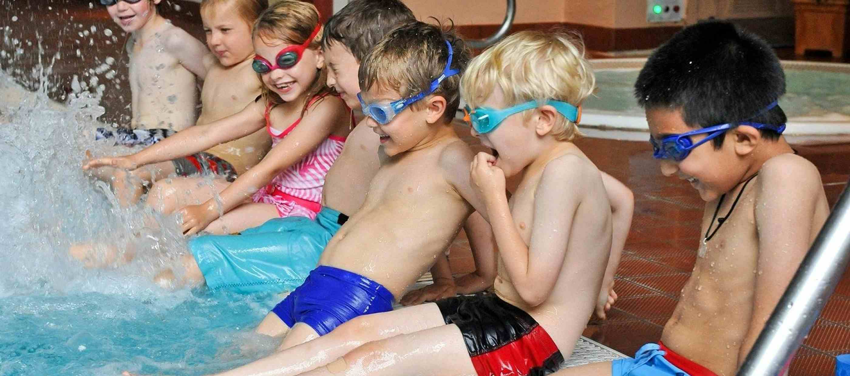 Children sitting on side of pool kicking their legs