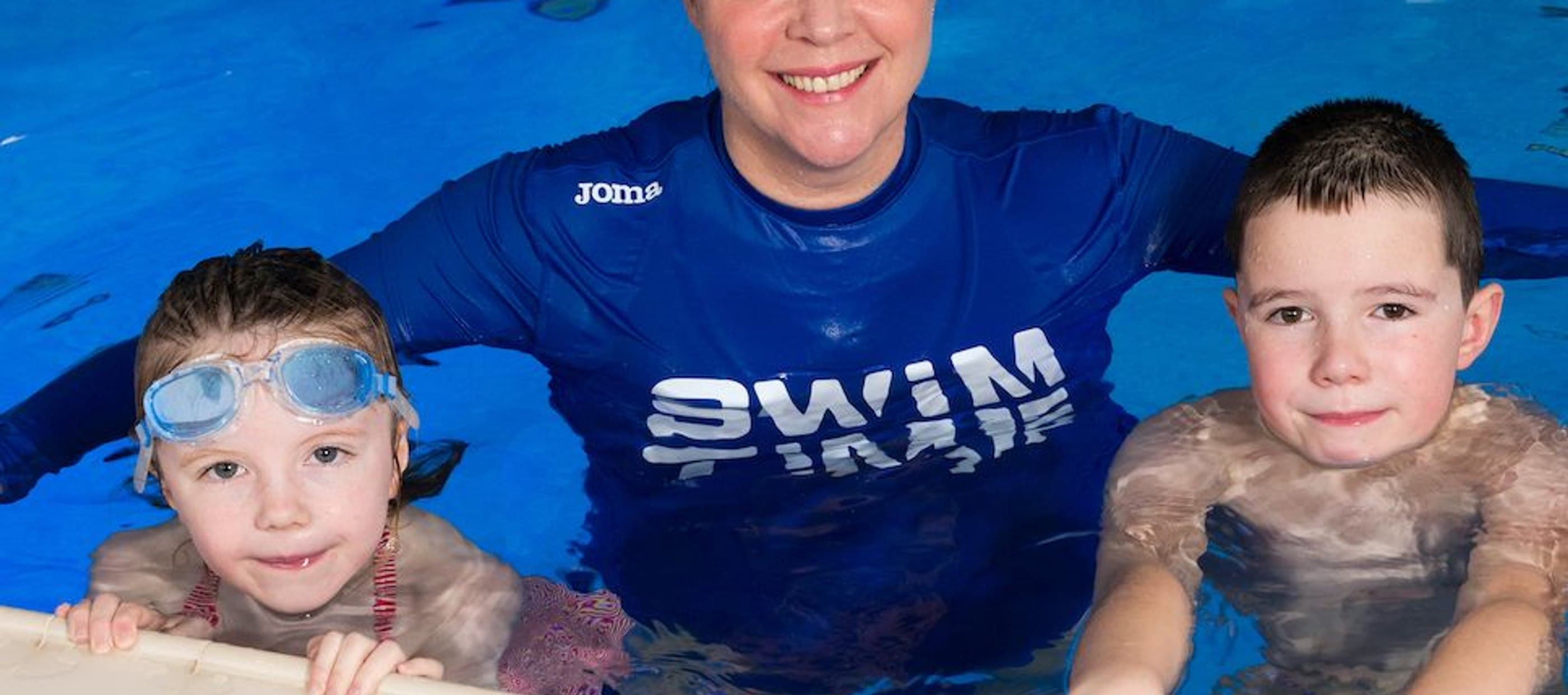 Instructor and children resting on side of swimming pool