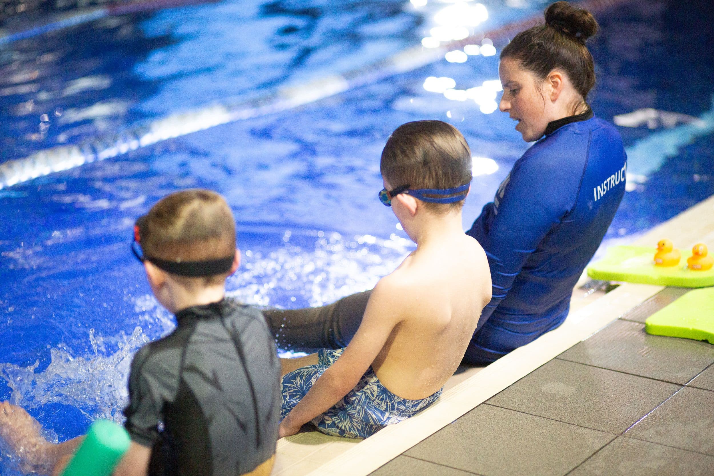 Instructor and swimmers kicking splashing water on edge of pool