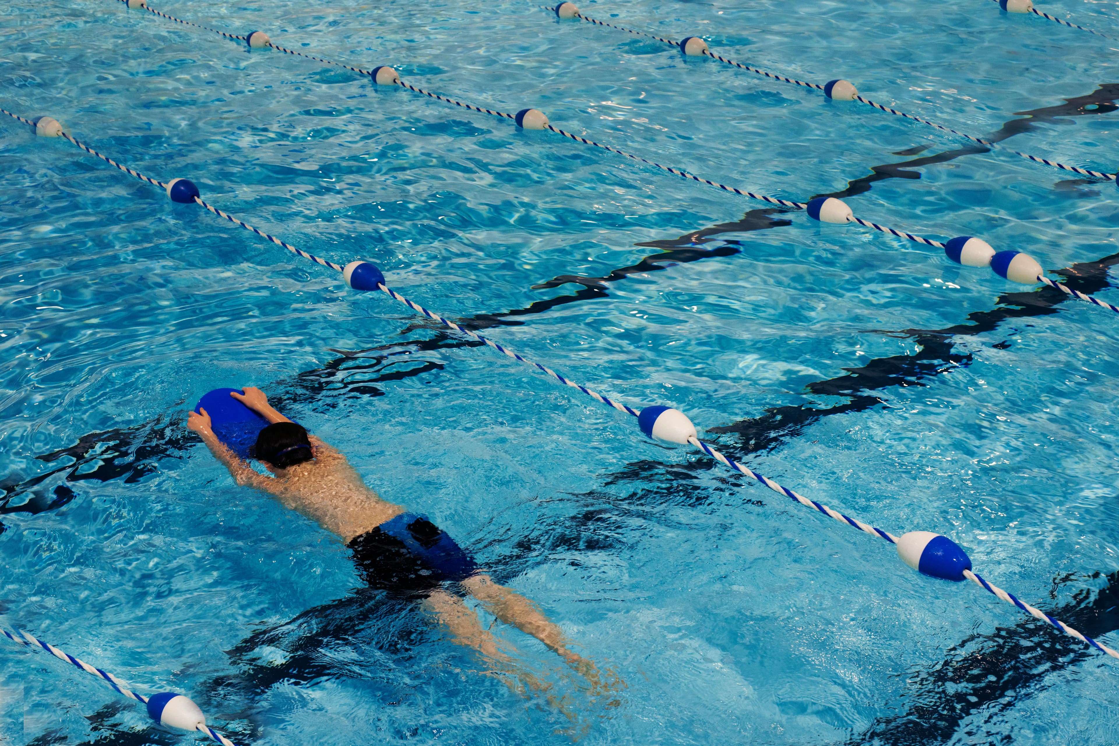 Child swimming in pool with kickboard